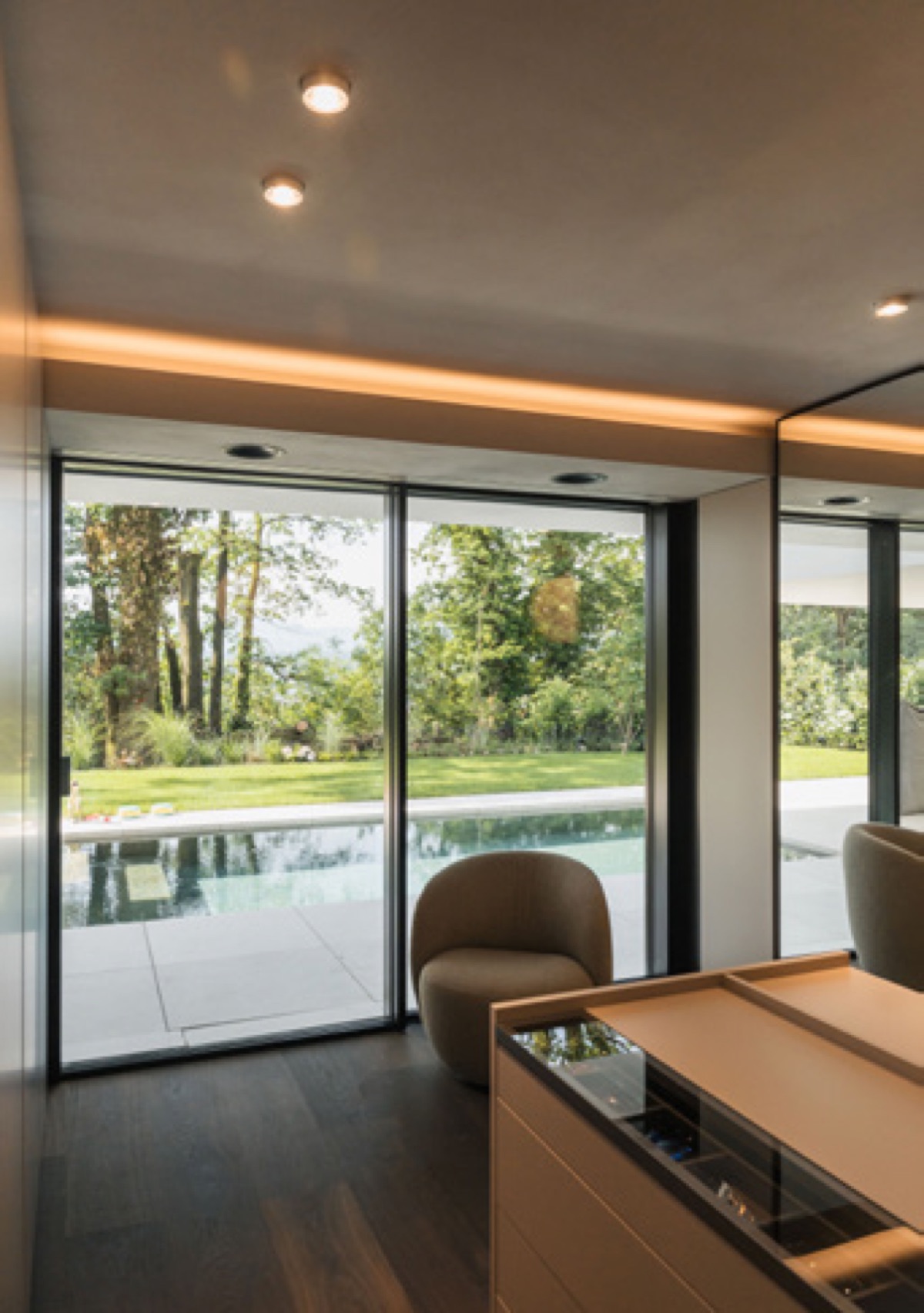 Architect-designed interior with floor-to-ceiling glazing, warm cove lighting, and pool view — Loxone climate controlled