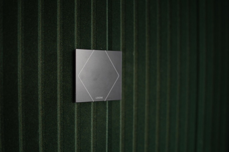 Loxone Touch wall switch mounted on textured green surface — precision lighting control